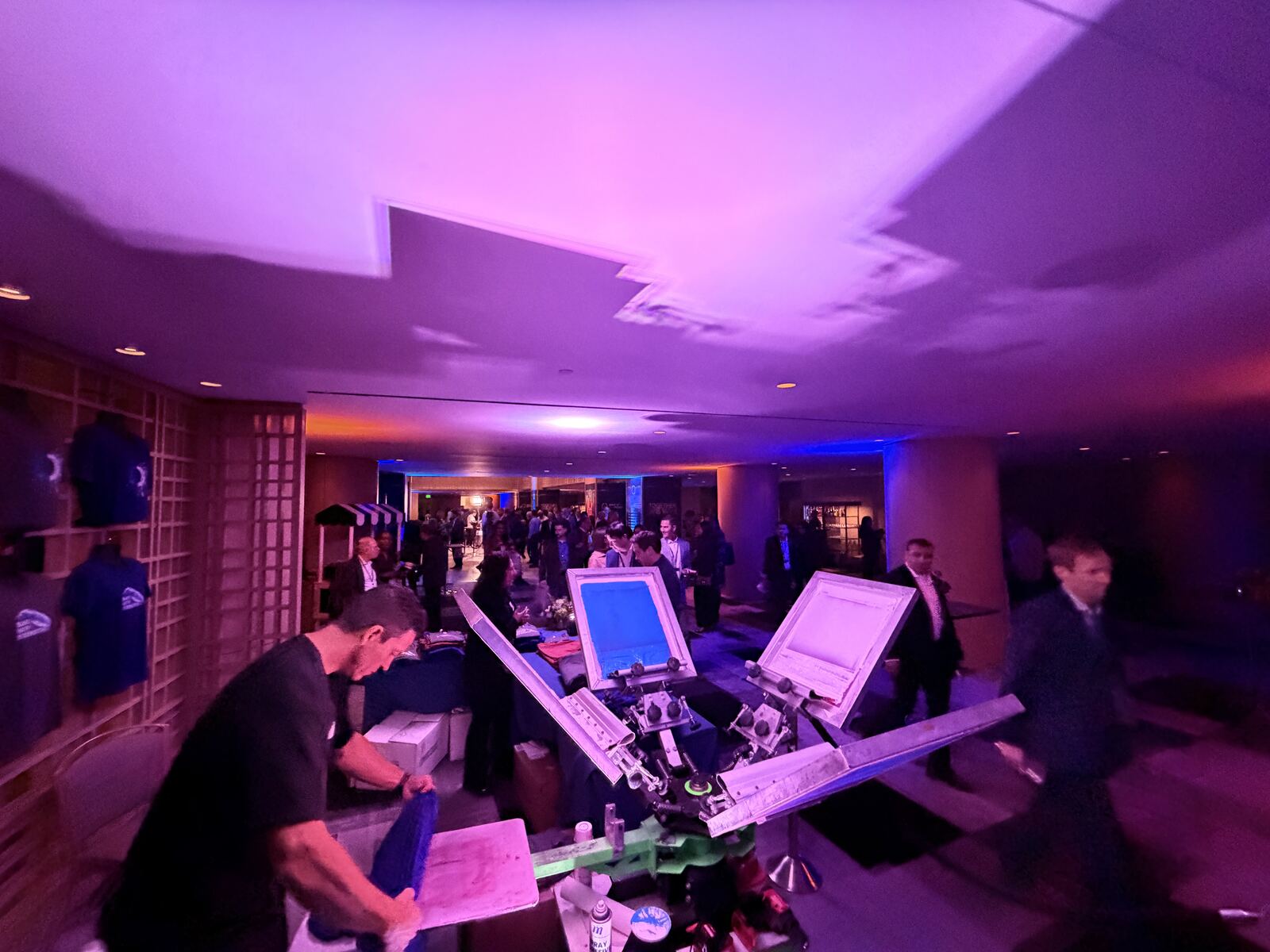 Professional event booth with multiple DTF printing machines and colorful sample t-shirts under purple and pink lighting
